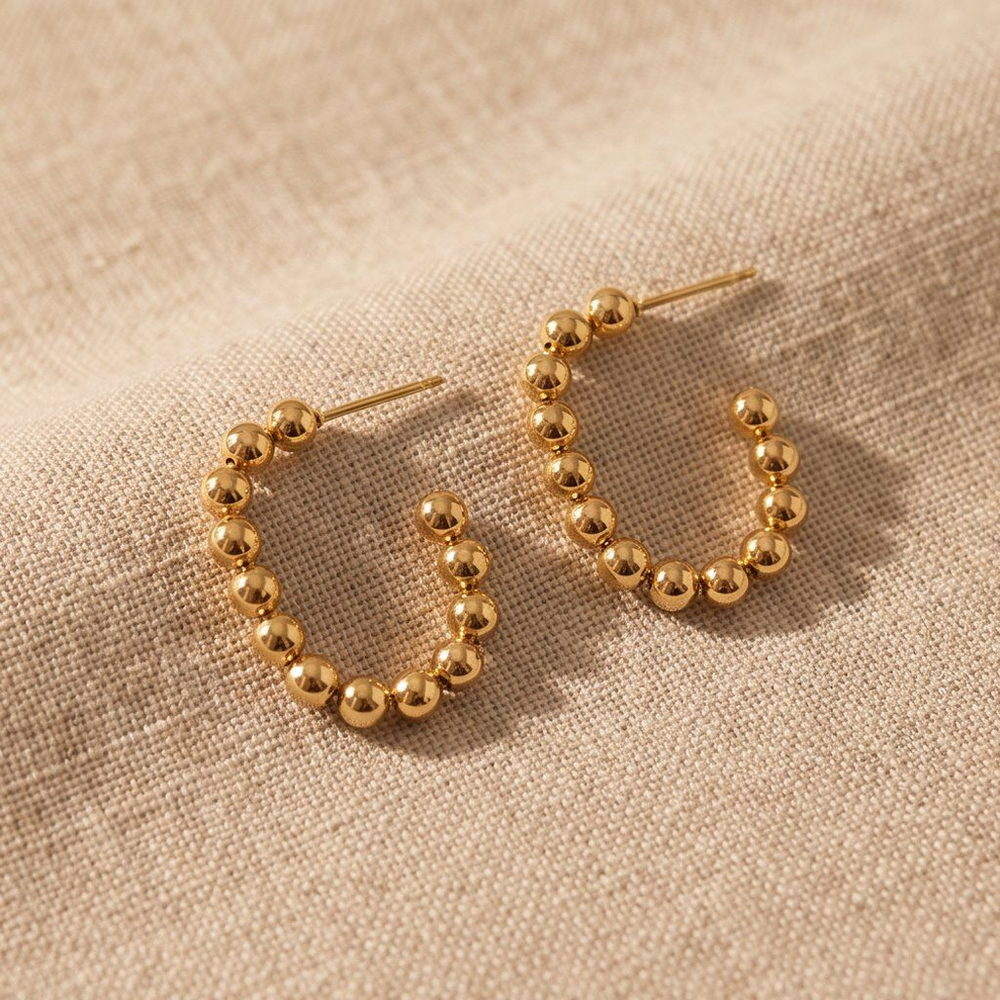 Gold-tone beaded huggie earrings with a row of small round beads along the outer face