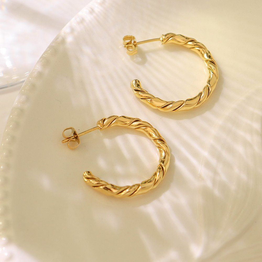 Small gold-tone croissant twist huggie hoop earrings shown as a pair on a pale surface