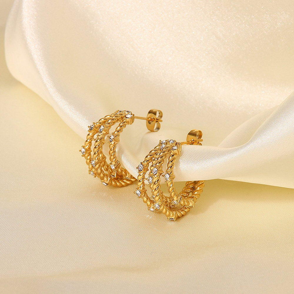 Multi-wire twisted gold-tone hoop earrings resting on cream silk