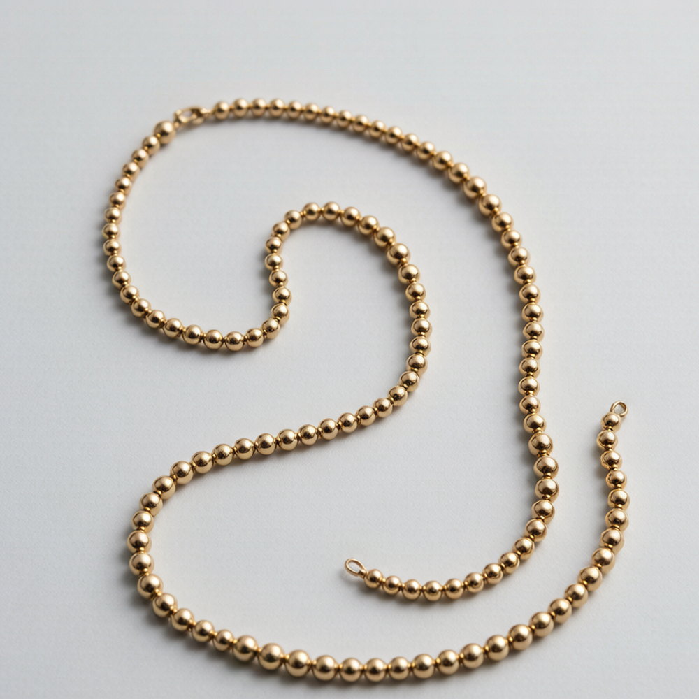 Fine gold-tone bead chain necklace coiled on a pale grey surface