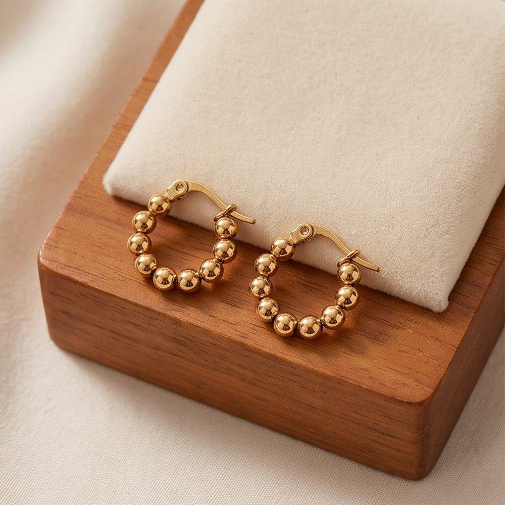 Two gold-tone bead-textured huggie earrings resting on a wooden block
