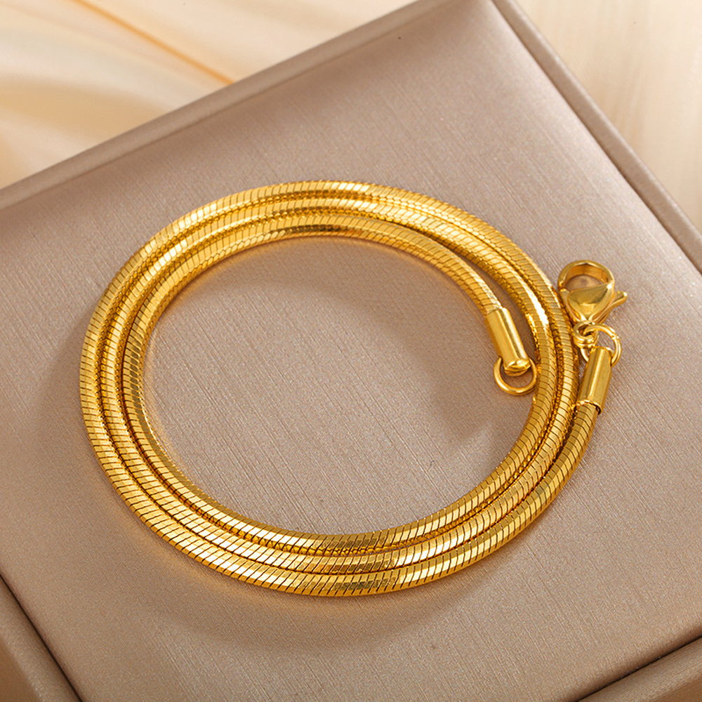 A multi-strand gold-tone snake chain necklace coiled on a pale surface