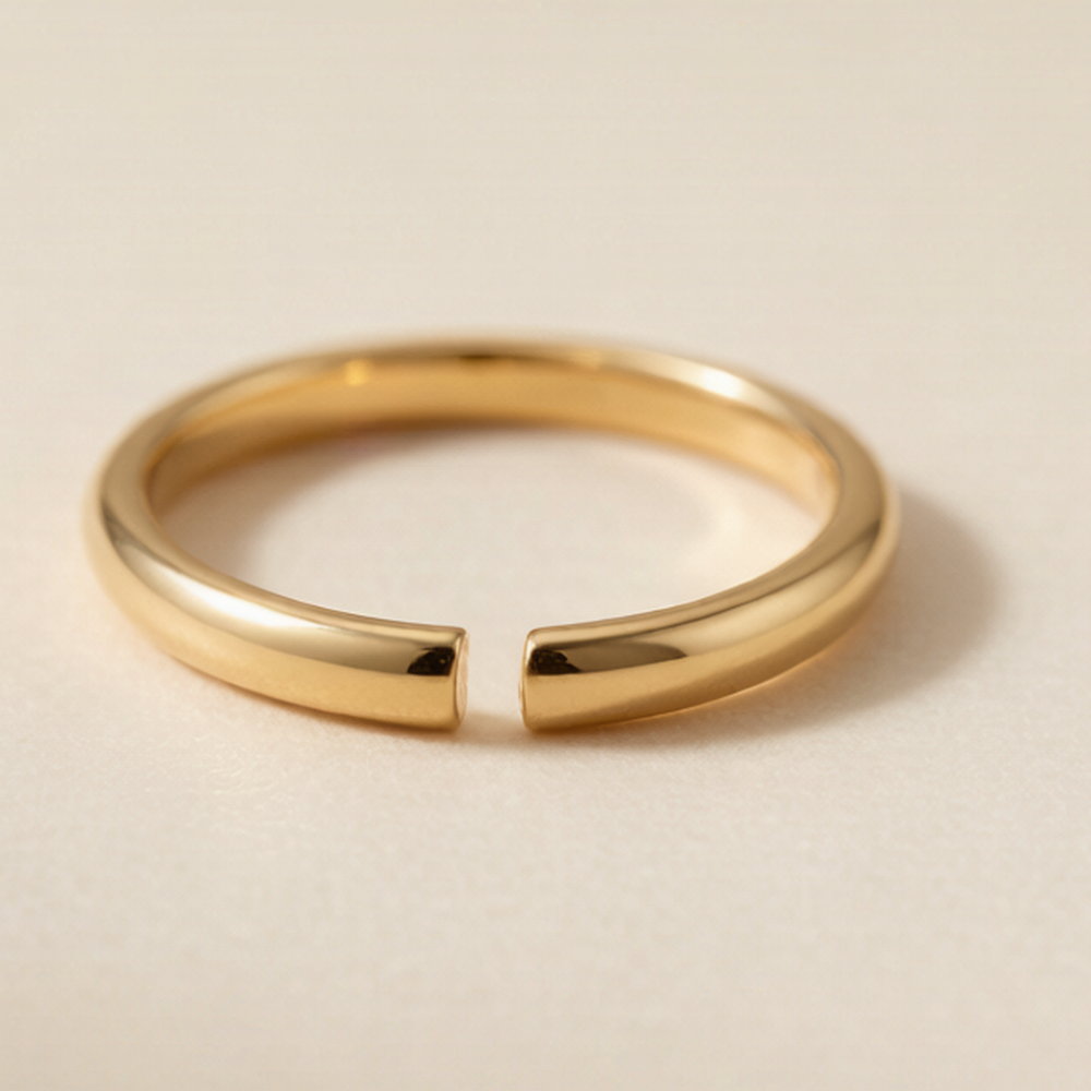 A plain polished gold-tone open adjustable ring with a narrow gap, resting flat on a pale surface