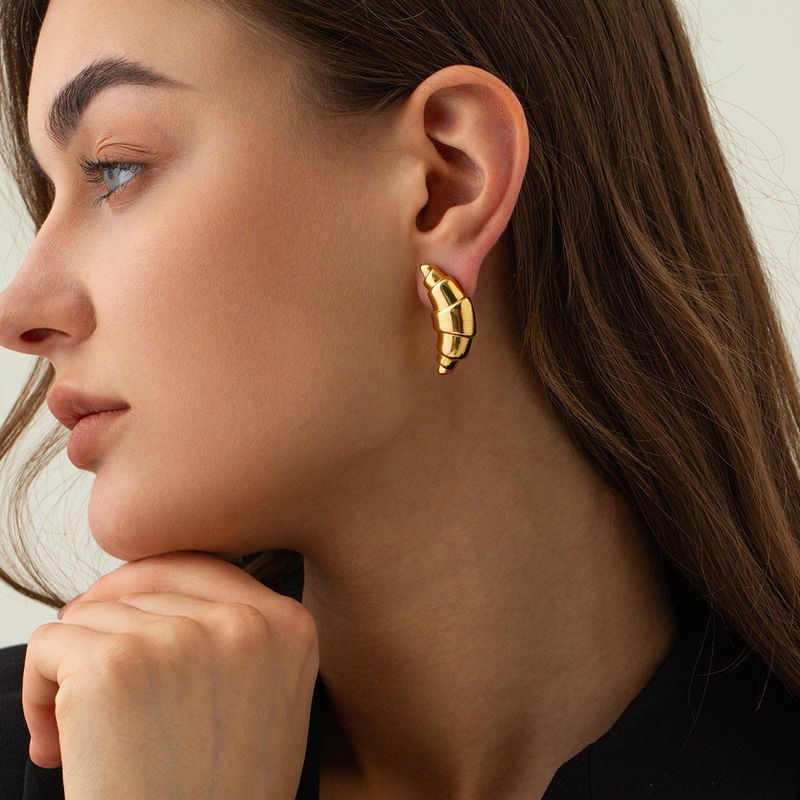 Model wearing a textured gold-tone earring, shown on the ear for scale