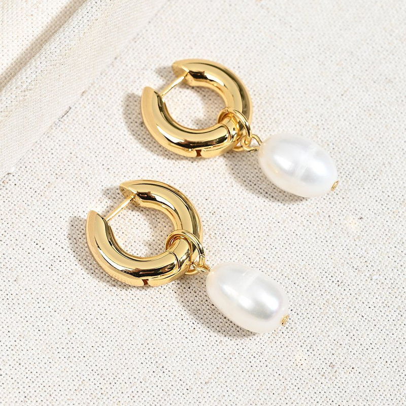 Gold-tone hoop earrings with large baroque pearl drops on a linen surface