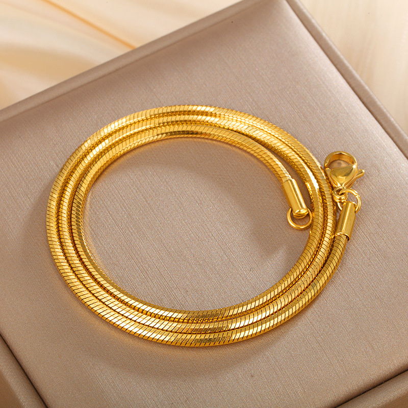 A flat snake chain necklace coiled on a pale surface, showing the flat link profile