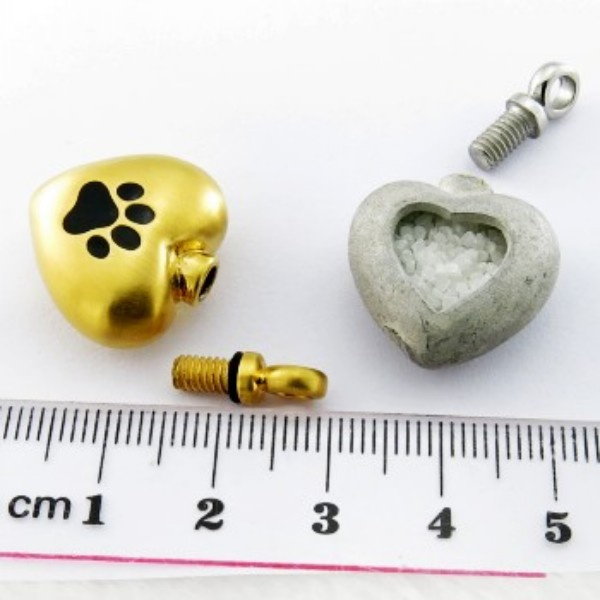 A gold-tone paw-print heart pendant with its screw plug removed, next to a stone keepsake heart and a centimetre ruler
